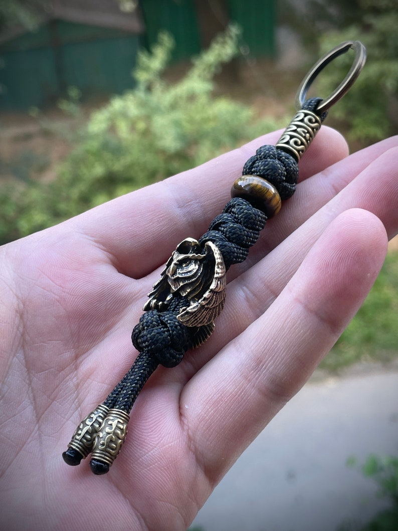 May include: A black paracord keychain with a brass owl charm, a tiger's eye bead, and a brass key ring.