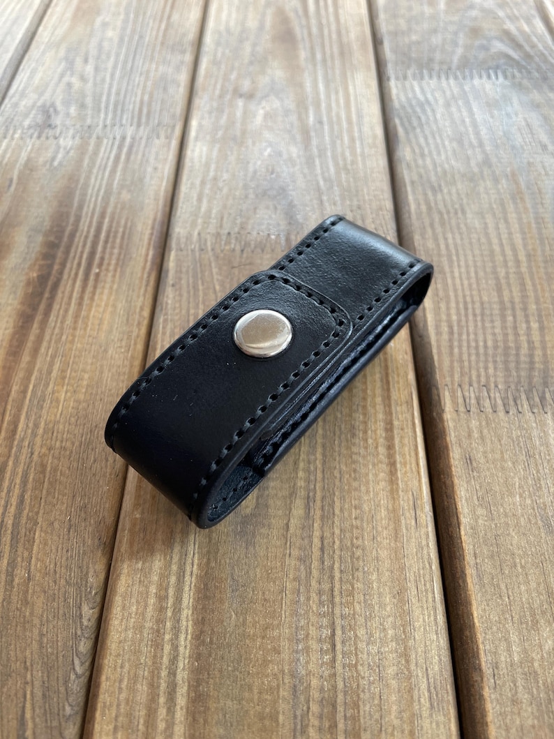 May include: A black leather case with a silver snap closure. The case is rectangular and appears to be stitched along the edges. The background is a wooden surface with visible grain.
