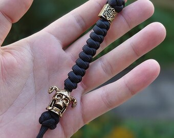 May include: Black paracord keychain with a gold skull bead and a gold Celtic knot bead.