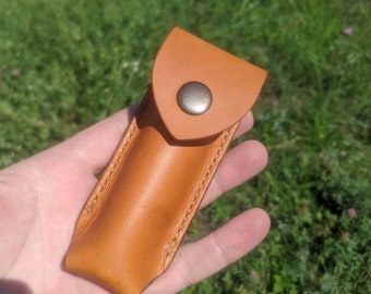May include: A brown leather case with a snap closure. The case is designed to hold a small, cylindrical object.