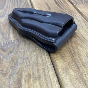 Peut inclure: Un étui en cuir noir avec un design moulé. L'étui est cousu sur les bords et semble être fait de cuir épais et durable. L'étui est conçu pour contenir une arme à feu.