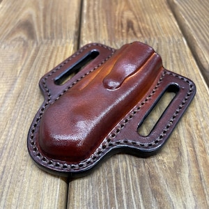 Peut inclure: Un étui à couteau en cuir marron fait à la main avec une finition brillante. L'étui est doté d'un clip de ceinture et est cousu avec du fil foncé sur les bords. Il comprend deux fentes pour la fixation à la ceinture.