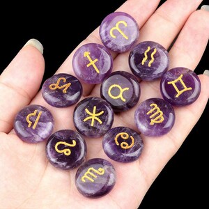May include: Set of 12 amethyst gemstone zodiac signs with gold lettering. Each stone is a different zodiac sign, including Aries, Taurus, Gemini, Cancer, Leo, Virgo, Libra, Scorpio, Sagittarius, Capricorn, Aquarius, and Pisces.