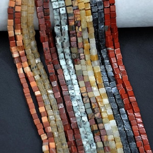 May include: A close-up of several strands of square beads in a variety of colours, including red, brown, grey, and yellow. The beads are strung together, creating a textured and colourful display. Suitable for jewellery making or crafts.