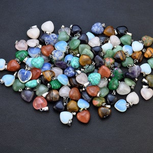Puede incluir: Un gran surtido de colgantes de piedras preciosas en forma de coraz&oacute;n en varios colores, incluyendo rosa, verde, azul, marr&oacute;n y morado. Los colgantes est&aacute;n hechos de piedras naturales y tienen lazos de metal plateados para sujetar a las joyas.