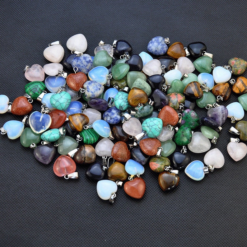 Puede incluir: Un gran surtido de colgantes de piedras preciosas en forma de coraz&oacute;n en varios colores, incluyendo rosa, verde, azul, marr&oacute;n y morado. Los colgantes est&aacute;n hechos de piedras naturales y tienen lazos de metal plateados para sujetar a las joyas.