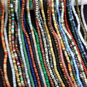 May include: A selection of colourful gemstone beads, including green, blue, red, brown, and white, are strung on thin cords. The beads are arranged in rows, creating a visually appealing pattern.