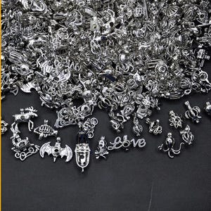 Könnte beinhalten: Eine große Sammlung von silbernen Anhänger-Anhängern, darunter Tier-, Herz- und Schädelmotive. Die Anhänger sind perfekt, um Schmuck eine persönliche Note zu verleihen.