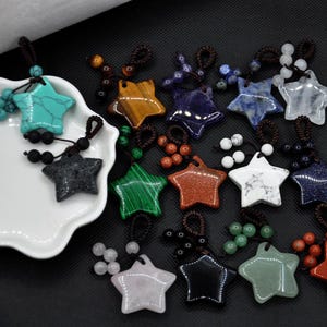 以下が含まれることがあります： 様々な色と素材の星型ペンダントのコレクション。 ターコイズ、黒、緑、白など。 各ペンダントは、茶色のコードに装飾ビーズを通してあり、ユニークで人目を引くアクセサリーになっています。