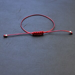 May include: A red string bracelet with silver beads at each end. The bracelet is tied with a knot in the center.