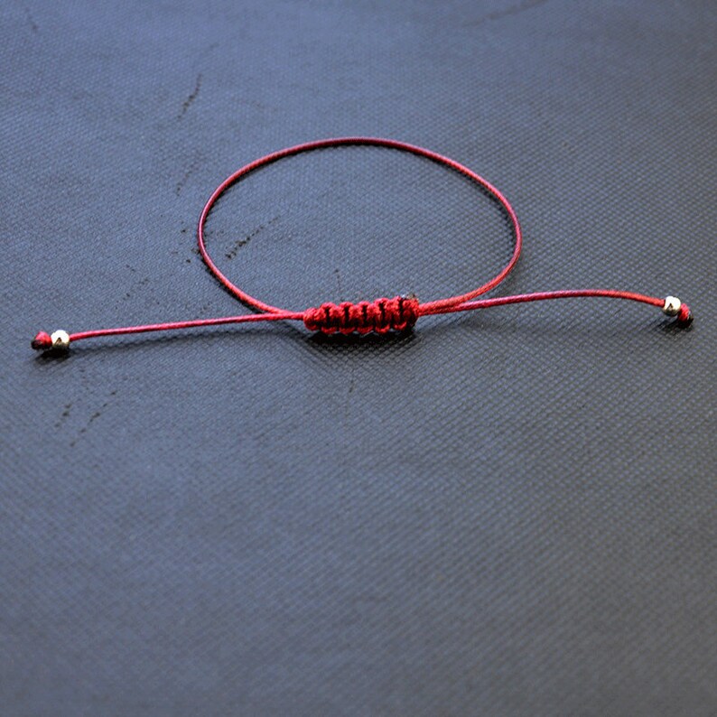 May include: A red string bracelet with silver beads at each end. The bracelet is tied with a knot in the center.