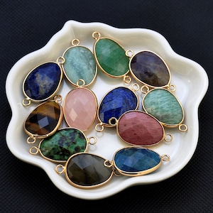 Könnte beinhalten: Sortiment an Edelstein-Anhängern mit goldfarbenen Metallösen. Die Edelsteine umfassen Lapislazuli, Tigerauge, Aventurin, Rosenquarz, Amethyst und mehr.