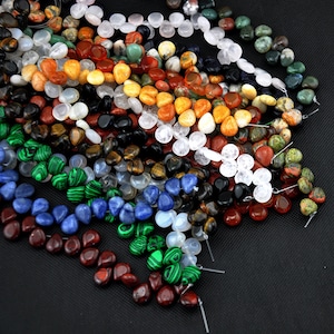 Pode incluir: Conjunto de contas de pedras preciosas em várias cores e formas, incluindo redondas, ovais e em forma de lágrima. As contas são enfiadas em um fio e estão prontas para serem usadas para a fabricação de joias.