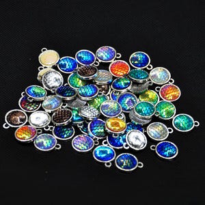 May include: A pile of small, oval pendants with iridescent, scale-like patterns in shades of blue, green, orange, and silver. Each pendant has a silver-coloured metal frame and a small loop for attaching to jewellery.