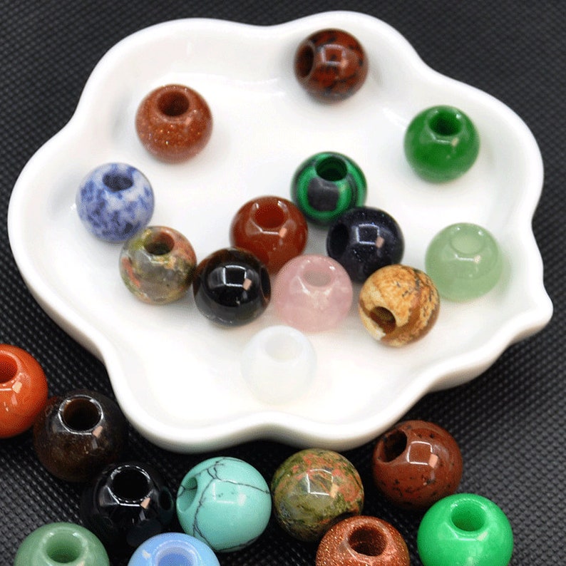 Puede incluir: Surtido de cuentas de piedras preciosas de colores con agujeros en el centro. Las cuentas son de varios tonos de verde, azul, rojo, marr&oacute;n, rosa y blanco. Las cuentas se muestran en un plato de cer&aacute;mica blanco.