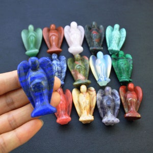 Könnte beinhalten: Eine Sammlung von 15 kleinen Engelsfiguren, die aus verschiedenen Edelsteinen geschnitzt sind, darunter Lapislazuli, Amethyst, Rosenquarz und grüner Aventurin. Die Figuren sind alle etwa 5 cm hoch und haben ein zartes, handgeschnitztes Aussehen.