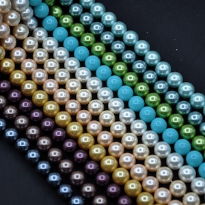 Könnte beinhalten: Eine Perlenschnur in verschiedenen Farben, darunter Weiß, Creme, Beige, Grau, Schwarz, Türkis und Grün. Die Perlen sind in Reihen angeordnet und bilden ein farbenfrohes und elegantes Display.