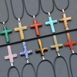 May include: Ten different coloured stone cross necklaces with black cords. The stones are turquoise, green, pink, blue, brown, red, orange, yellow, and white.