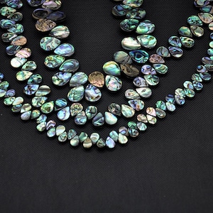 May include: Multiple strands of teardrop-shaped abalone shell beads arranged in a curved pattern. Each bead displays a natural iridescent finish with swirling hues of green, blue, purple, and brown, reflecting light across their polished surfaces.