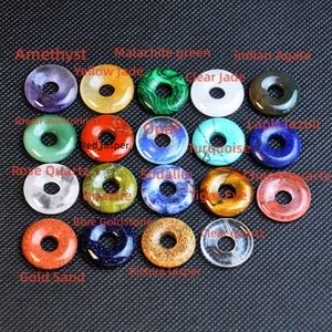 May include: Assortment of 18 donut-shaped gemstone rings in various colors, including amethyst, yellow jade, malachite green, clear jade, green aventurine, red jasper, opal, turquoise, lapis lazuli, rose quartz, sodalite, tiger eye, cherry quartz, blue goldstone, picture jasper, and clear quartz.