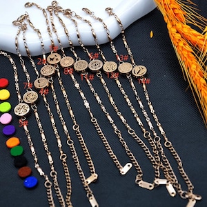 May include: Gold-coloured bracelets with decorative circular pendants featuring various etched designs. The bracelets are displayed on a white surface with a dark background. Colourful felt pads are visible on the left side of the image.