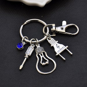 May include: Silver keychain with a blue rhinestone, a lightbulb, a screwdriver, and a plug with the word "electrified" on it.