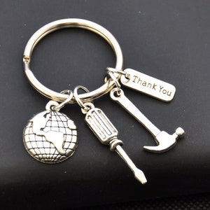 Puede incluir: Llavero plateado con un globo terráqueo, un destornillador, un martillo y una etiqueta que dice "Gracias".