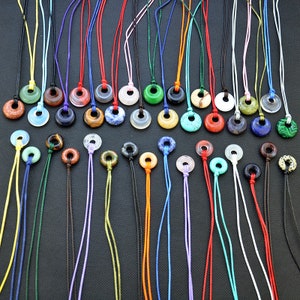 Puede incluir: Una colección de 30 colgantes de anillo de piedras preciosas de colores en cordones ajustables. Los colgantes están hechos de varias piedras, incluyendo ágata, jaspe, turquesa y lapislázuli. Cada colgante es de un color y un patrón diferente.