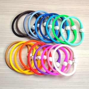 May include: A set of 20 colourful silicone bracelets with a pearl accent. The bracelets are arranged in a rainbow pattern, with the colours ranging from brown to white.