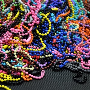 May include: A large pile of colorful plastic bead chains. The chains are in various colors, including red, blue, green, yellow, orange, pink, and purple. The chains are all about the same size and are made of small, round beads.