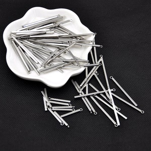 May include: A pile of silver metal bar connectors with small loops at each end. The connectors are arranged in a white dish and scattered on a black surface.