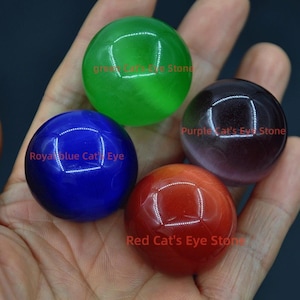 May include: Four polished gemstone spheres in green, blue, red, and purple. Each sphere has a cat's eye effect and is labeled with its color: "Royal Blue Cat's Eye", "Green Cat's Eye Stone", "Red Cat's Eye Stone", and "Purple Cat's Eye Stone".