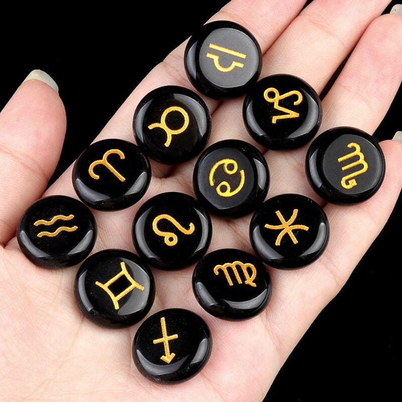 May include: Twelve black gemstone zodiac signs with gold lettering. The signs are arranged in a circle on a hand.