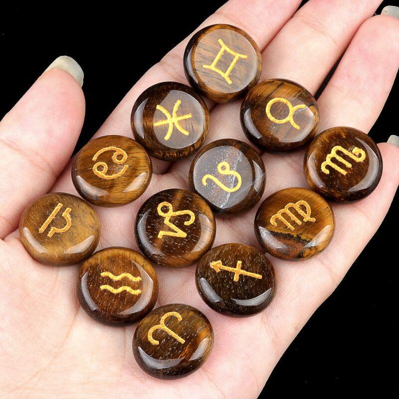 May include: Twelve tiger's eye stones, each with a different zodiac symbol engraved in gold. The stones are arranged in a circle on a hand.