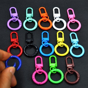 Op de afbeelding: Assortiment van 14 kleurrijke metalen sleutelhangers met draaibare clips en ronde ringen. De sleutelhangers zijn in verschillende kleuren verkrijgbaar, waaronder paars, turquoise, oranje, wit, roze, rood, zwart, blauw, geel, bruin en groen.