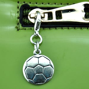 May include: A silver football charm hangs from a silver chain attached to a zipper pull on a green bag.