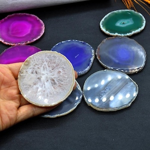 May include: A collection of polished agate slices in various colors, including purple, blue, green, and gray. The slices are round and display natural patterns and crystal formations. Some slices have a polished edge.