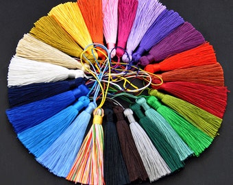 May include: A collection of colorful tassels arranged in a circular pattern. The tassels are made of silky threads in various colors, including yellow, orange, pink, purple, and green. The tassels are tied together with thin cords.