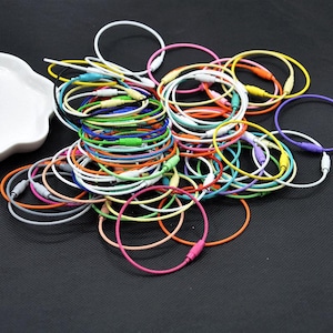 May include: A large pile of colorful metal key rings. The key rings are made of a thin, flexible metal and are available in a variety of colors, including red, blue, green, yellow, orange, purple, and white.