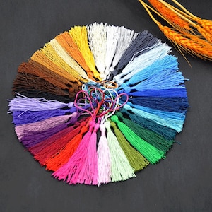 May include: A collection of colorful tassels in various shades, including red, pink, green, blue, and yellow. The tassels are arranged in a circular pattern, with a central knot of string. The image showcases a variety of craft supplies.