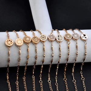 Puede incluir: Diez pulseras doradas con diferentes dijes decorativos. Cada pulsera presenta una cadena delicada y un dije redondo con un diseño único, que incluye una flor, un árbol de la vida y un mandala.