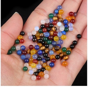 May include: A collection of colorful gemstone beads in various shapes and sizes, including round, oval, and teardrop. The beads are made of natural stones such as agate, amethyst, tiger's eye, and lapis lazuli.
