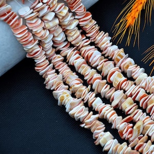 Peut inclure: Cinq brins de perles plates, irrégulières et en forme de disque dans des tons de blanc, crème et orange corail doux. Chaque perle présente une surface lisse et polie avec des variations naturelles de couleur et de forme, enfilées sur des fils.