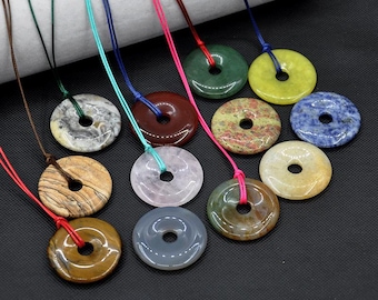 May include: A collection of gemstone pendant necklaces. Each necklace features a circular, donut-shaped pendant in various colors and patterns, including green, brown, and blue. The pendants are strung on colorful cords.