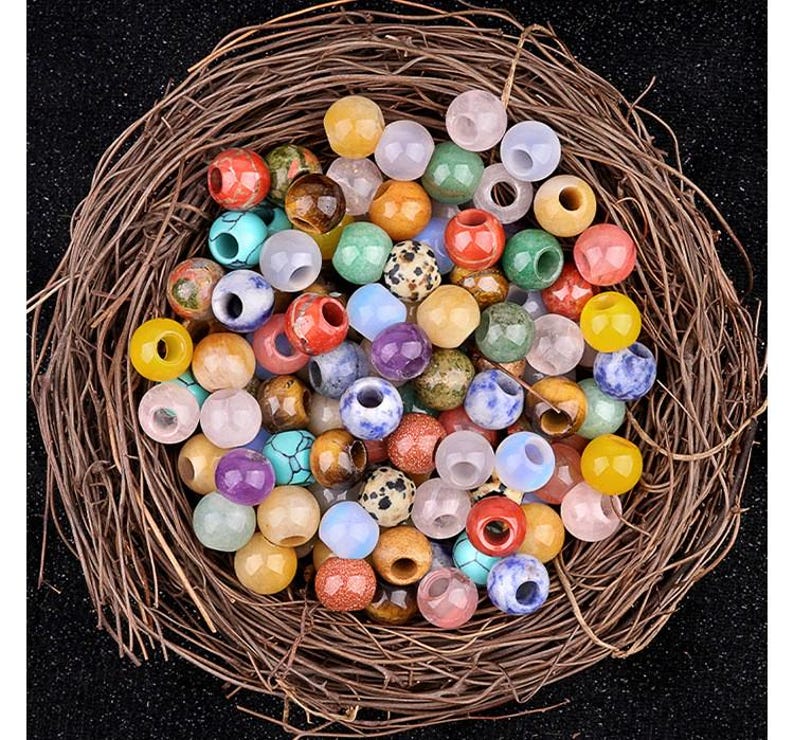 Puede incluir: Una colecci&oacute;n de cuentas de piedras preciosas de colores en varias formas y tama&ntilde;os. Las cuentas est&aacute;n dispuestas en un entorno similar a un nido, mostrando su belleza natural y sus patrones &uacute;nicos.