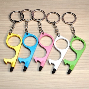 Könnte beinhalten: Fünf mehrfarbige berührungslose Schlüsselanhänger-Werkzeuge. Jedes Werkzeug hat eine kreisförmige Öffnung, einen Haken und eine Stiftspitze. Zu den Farben gehören Gelb, Blau, Rosa, Weiß und Grün. Die Schlüsselanhänger sind an silbernen Schlüsselringen befestigt.