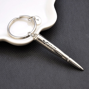 Puede incluir: Llavero de bala de plata con un anillo de plata y un pequeño dije de plata con la letra A. La bala tiene las palabras "CROSS FAMILY" grabadas.