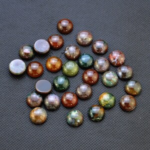 May include: A collection of 25 round, multi-colored agate cabochons. The cabochons are approximately 1 inch in diameter and feature a variety of colors, including brown, green, red, and white.