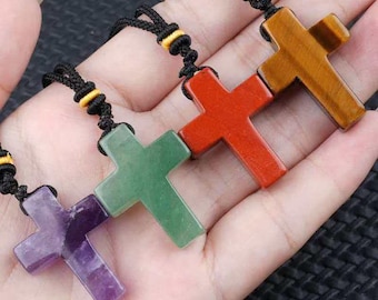 May include: A selection of gemstone cross pendants in shades of purple, green, red, and brown. Each cross is suspended on a black cord with yellow detailing, highlighting the natural colours of the stones.
