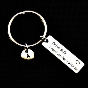May include: Silver keychain with a small charm with the letter A and a rectangular tag that reads "Drive Safe I need you here with me" with a heart symbol.